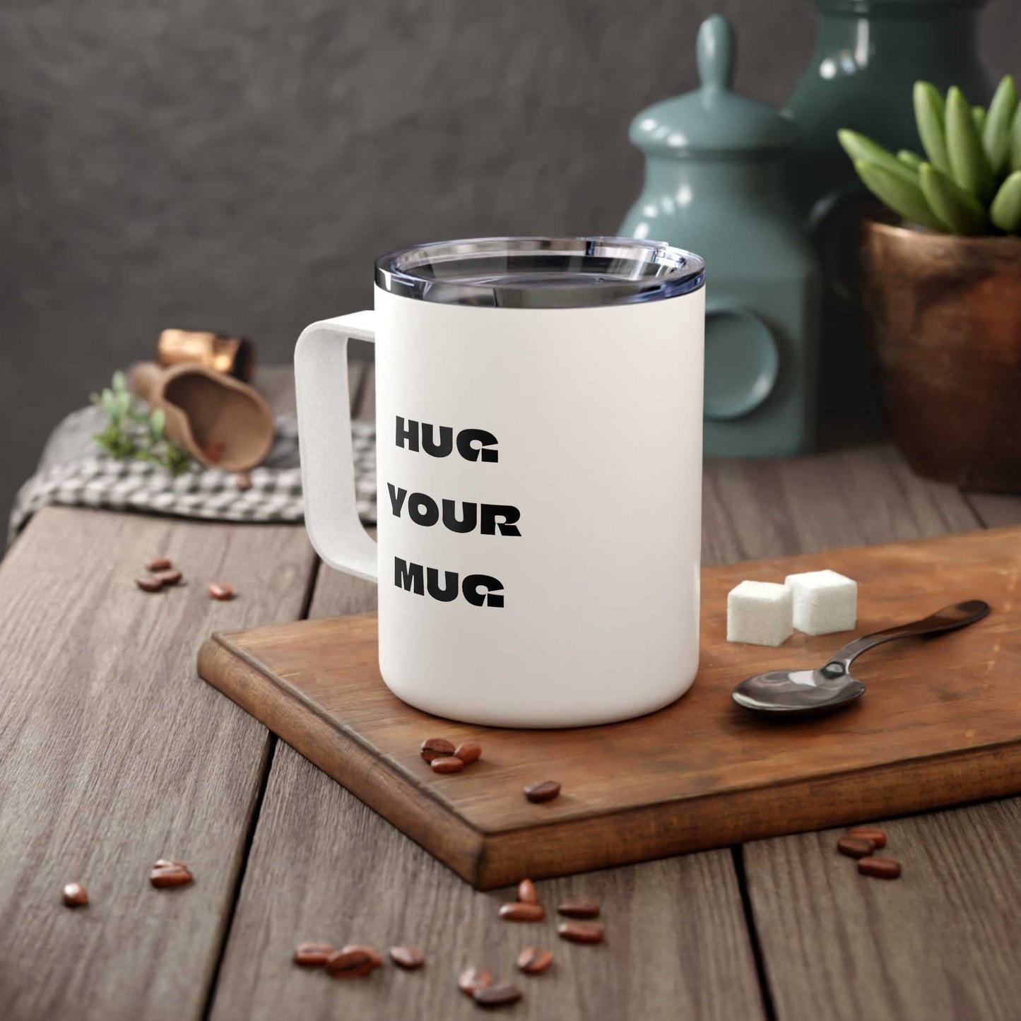 White mug with 'HUG YOUR MUG' text on a wooden surface with coffee beans and sugar cubes.