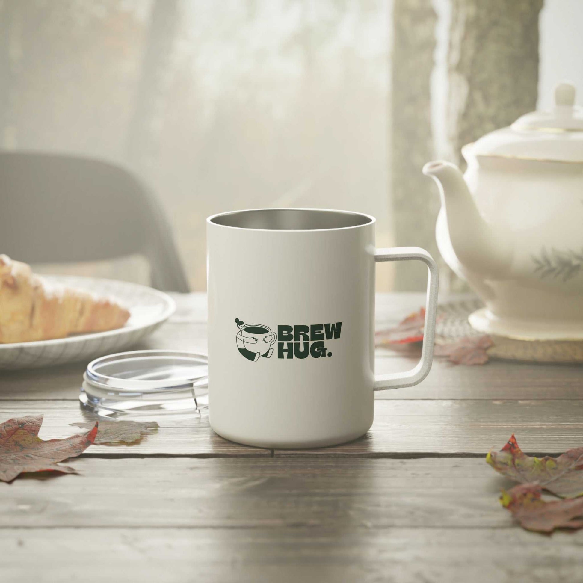 White mug with 'Brew Hug' text on a wooden table with a teapot and bread in the background.