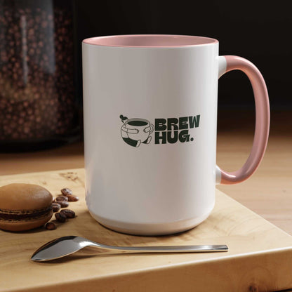 White mug with pink handle featuring 'Brew Hug' text on a wooden surface with coffee beans and a macaron.