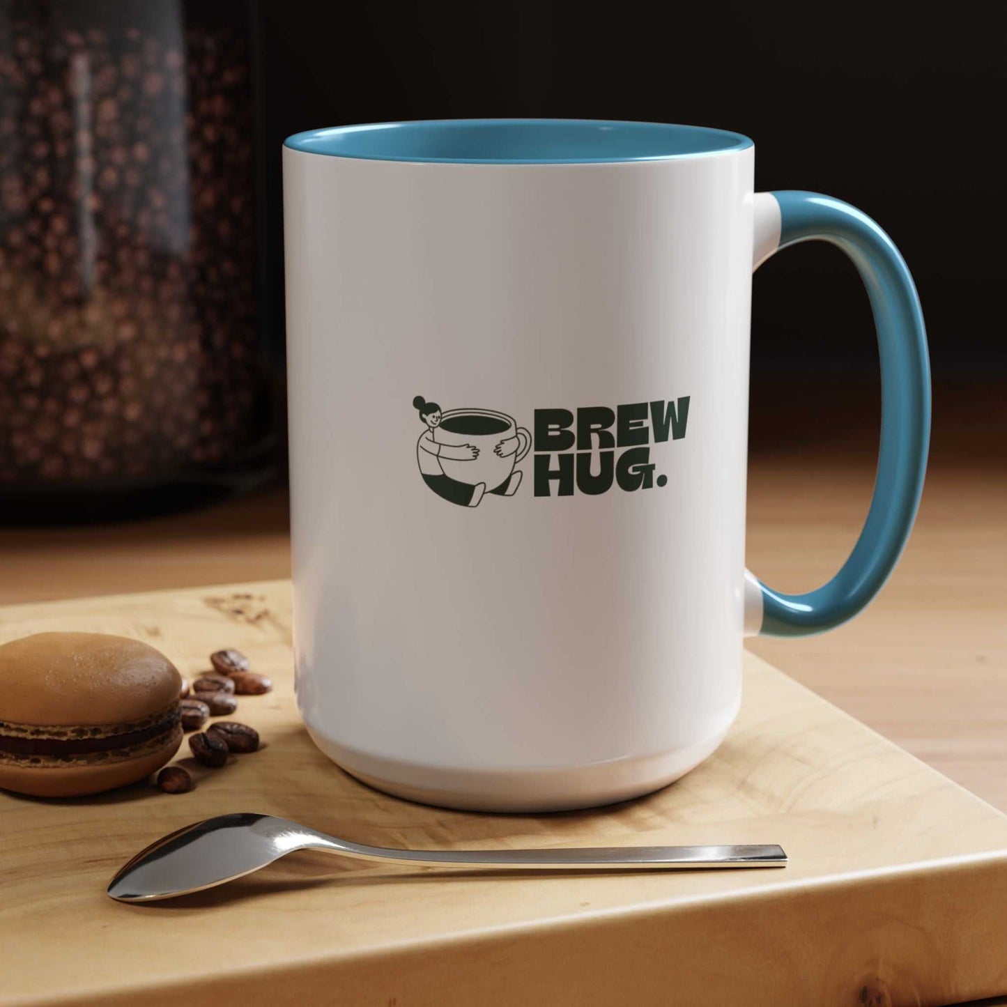 White mug with blue interior and handle, featuring 'Brew Hug' text, on a wooden surface with coffee beans and a spoon.