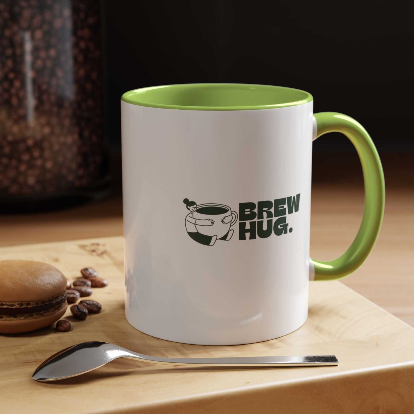 White mug with green interior and handle, featuring 'Brew Hug' text, on a wooden surface with coffee beans and a spoon.