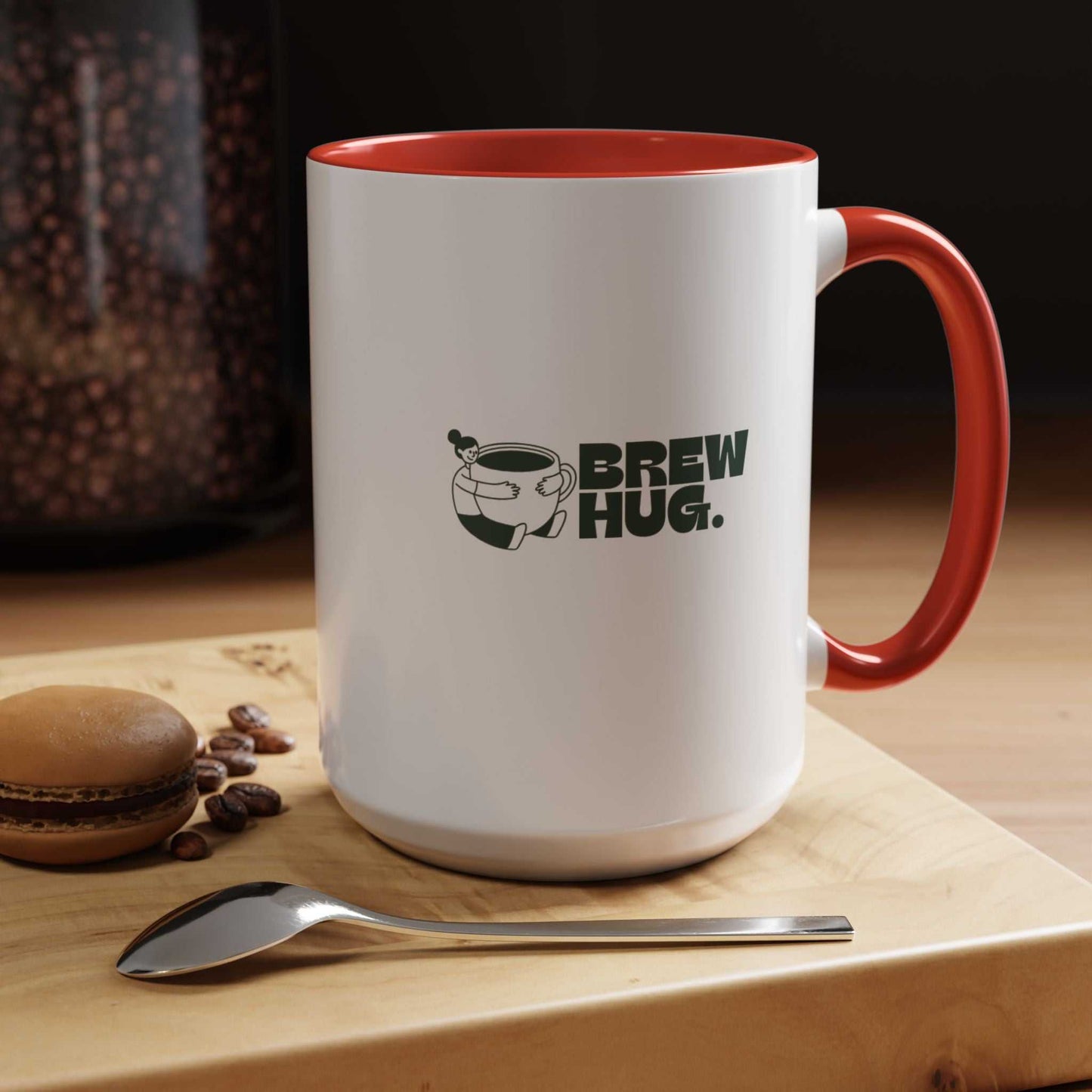 White mug with red interior and handle, featuring 'Brew Hug' text and coffee bean graphic, on a wooden surface with coffee beans and a spoon.